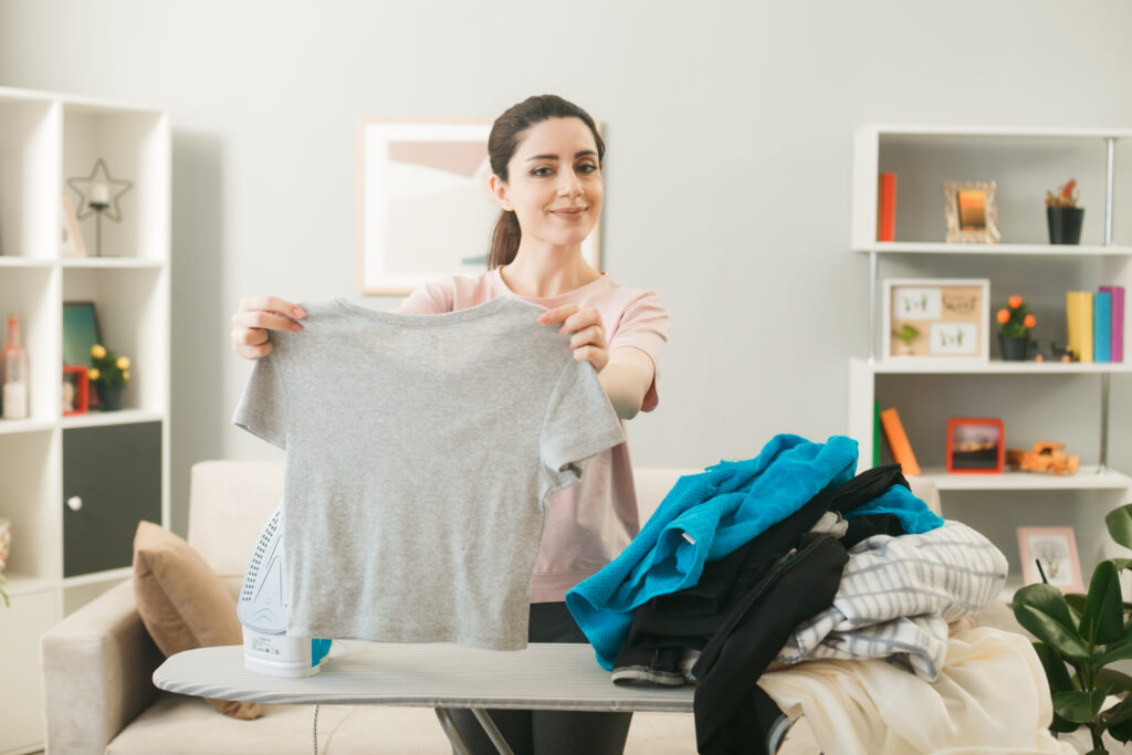 young girl standing ironing board with clothes living room